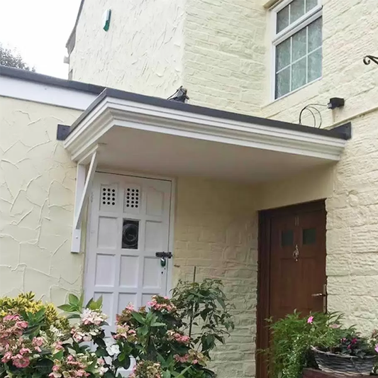 Front of a house with a white door and brown door, surrounded by flowers and plants, with an overdoor canopy covering both entrances.